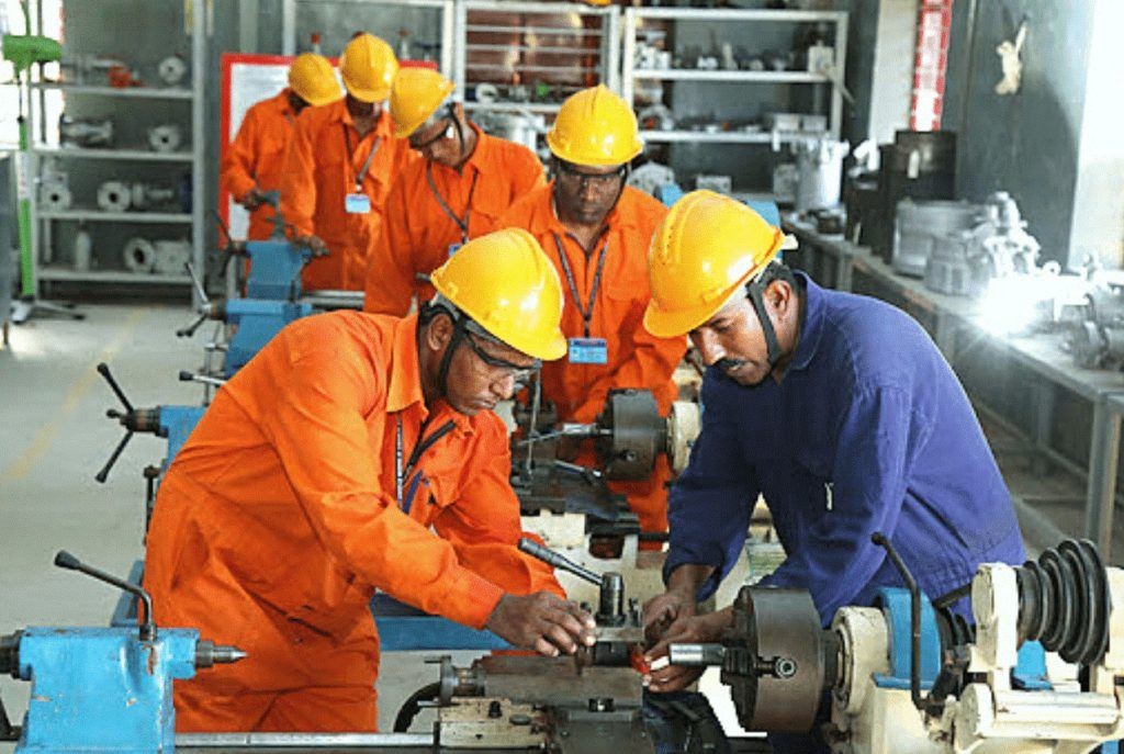 Workers in orange safety uniforms and hard hats operating machinery in an industrial workshop.
