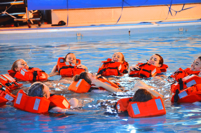Group of people wearing red life vests floating in a swimming pool during a safety training exercise.