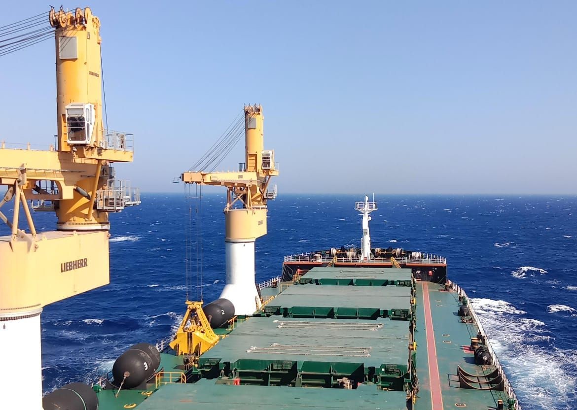 View from the deck of a cargo ship at sea, showing cranes and ocean horizon.