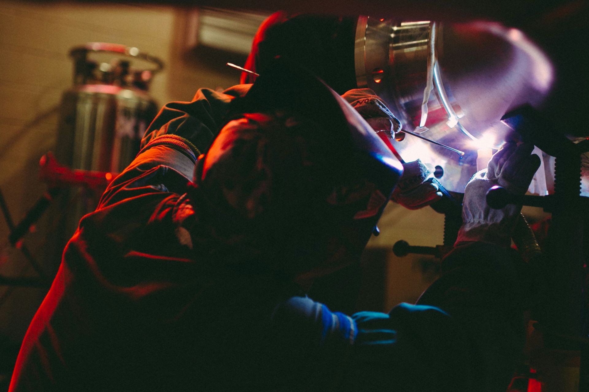 Person in protective gear welding metal with bright sparks and intense light, in an industrial setting.