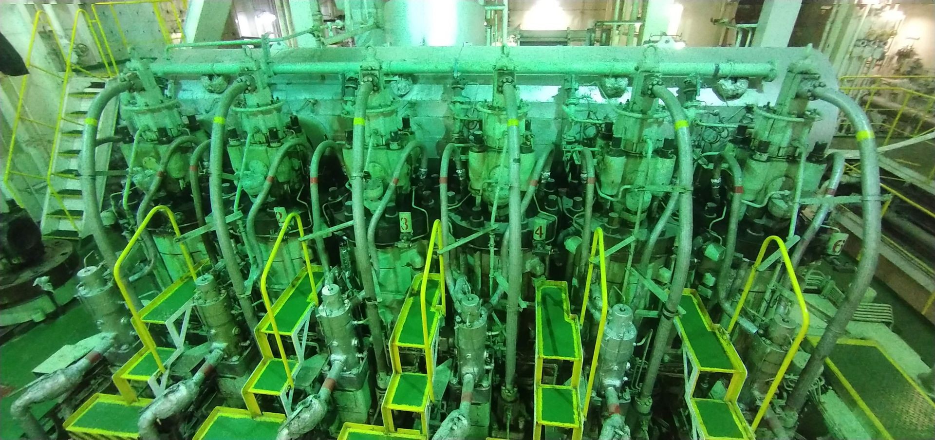 Industrial machinery with several connected pipes and yellow railings, inside a large facility.
