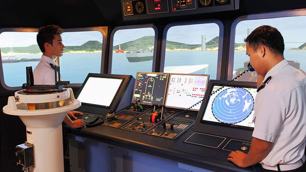 Two officers operating ship's navigation controls on a bridge simulator with ocean view outside.
