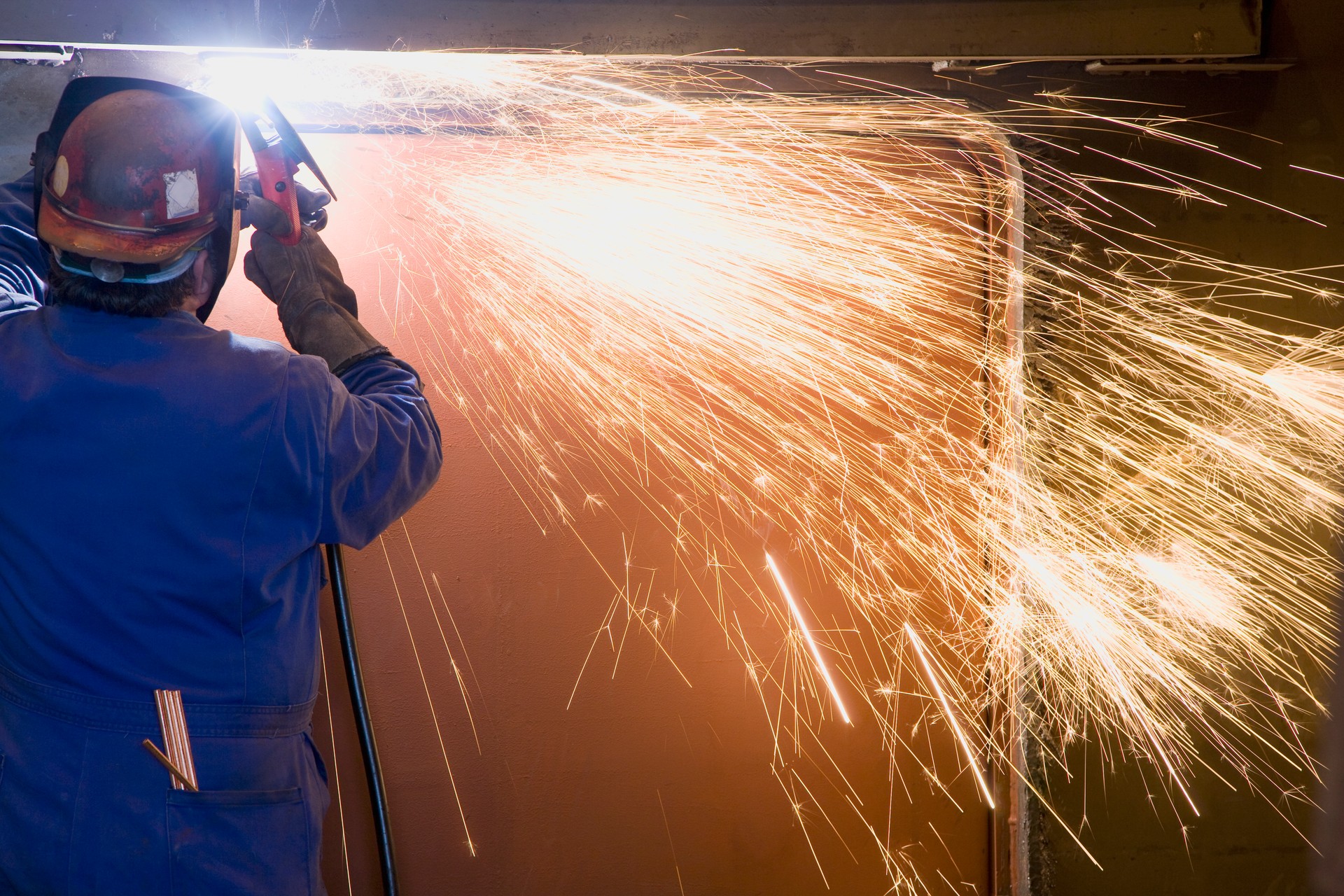 Welder welding side of boat hull in machine shop